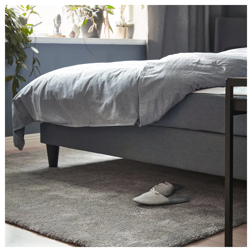Bedroom with grey STOENSE rug, black bed, and slippers; soft, textured floor covering.