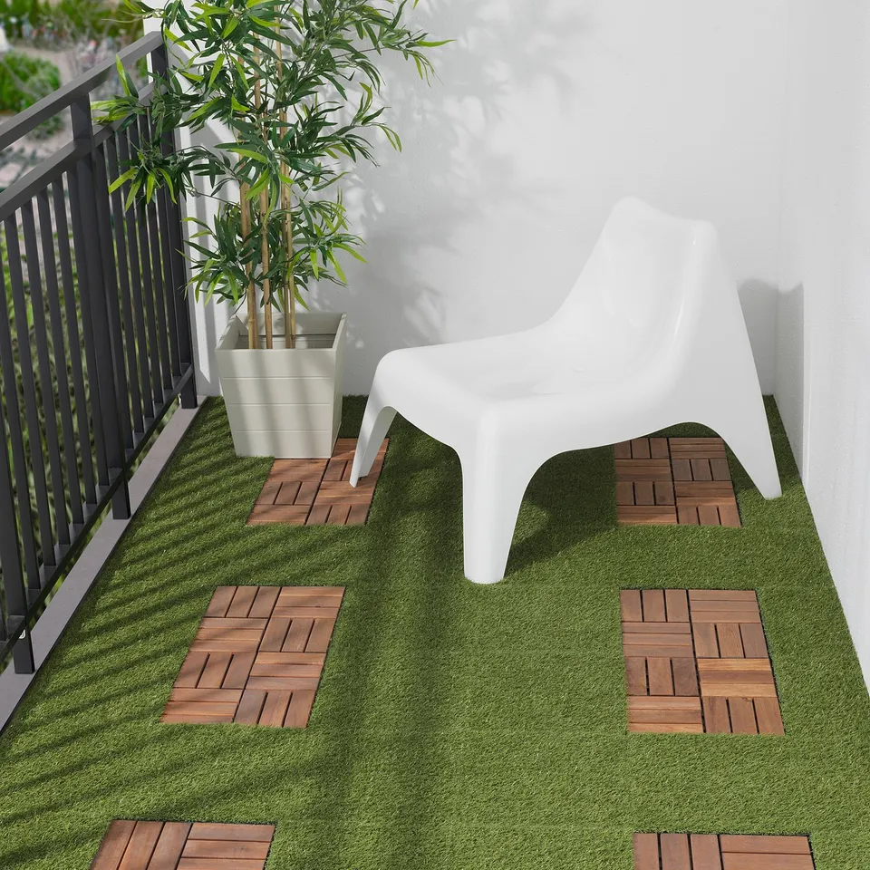 RUNNEN white chair on small brown tile path, large plant nearby, balcony.