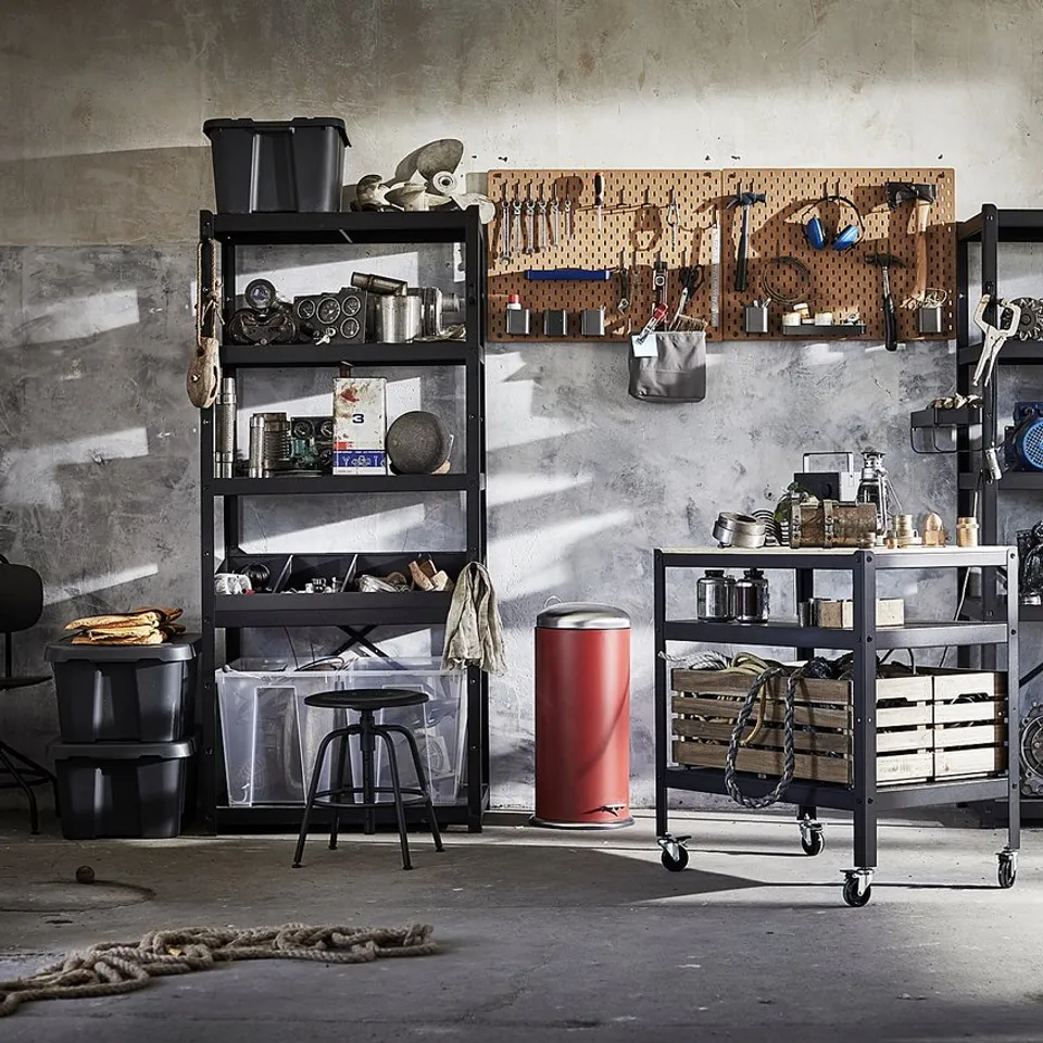 Industrial storage room with black metal BROR shelves, holding various tools and items, and a red trolley with castors.