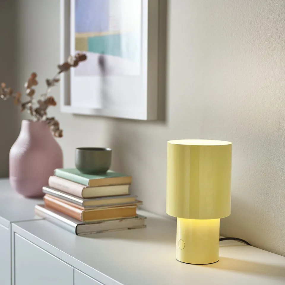 Yellow SPETSBOJ lamp on cabinet with books and plant.