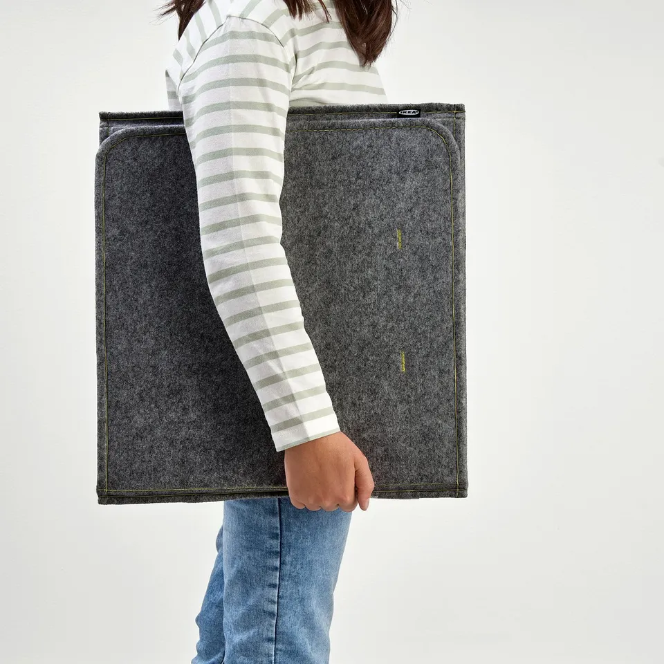 A person holding an ÖVNING desk divider, a portable privacy screen with a sound-absorbing material and side compartments.