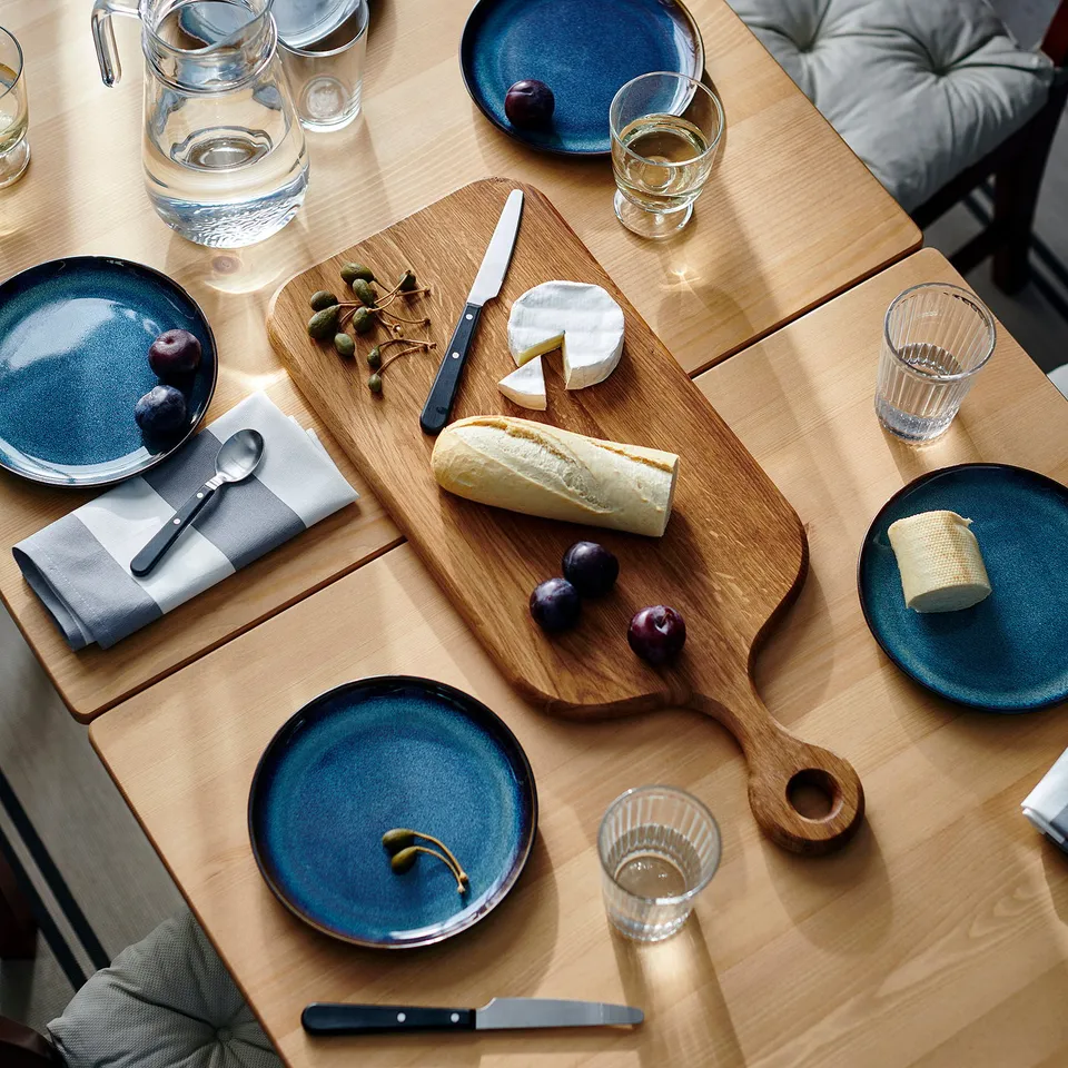 ARTISTISK chopping board, wooden, rectangular, placed on table with plates, glasses, and cheese. Large, central in setup.