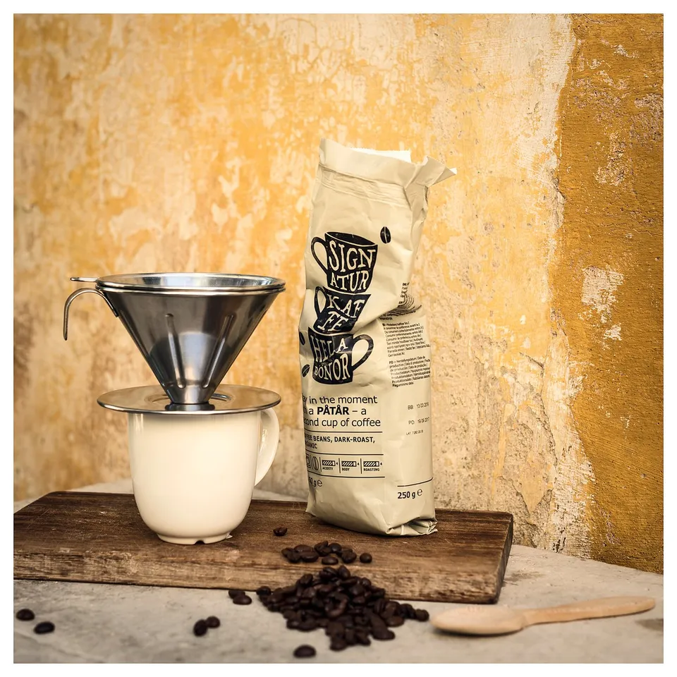 Stainless steel coffee philtre, white mug, and coffee beans on wooden board.