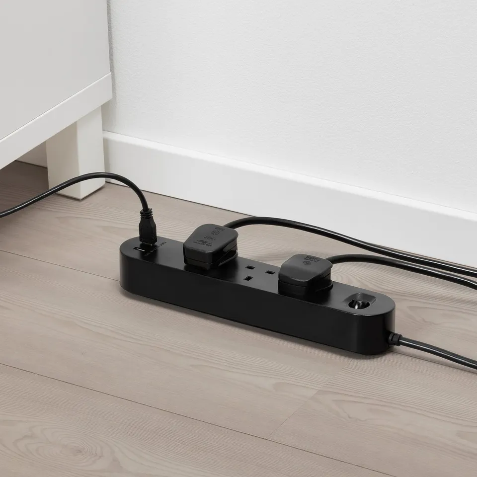 Black multi-socket adapter with 3 outlets and 2 usb ports on wooden floor.