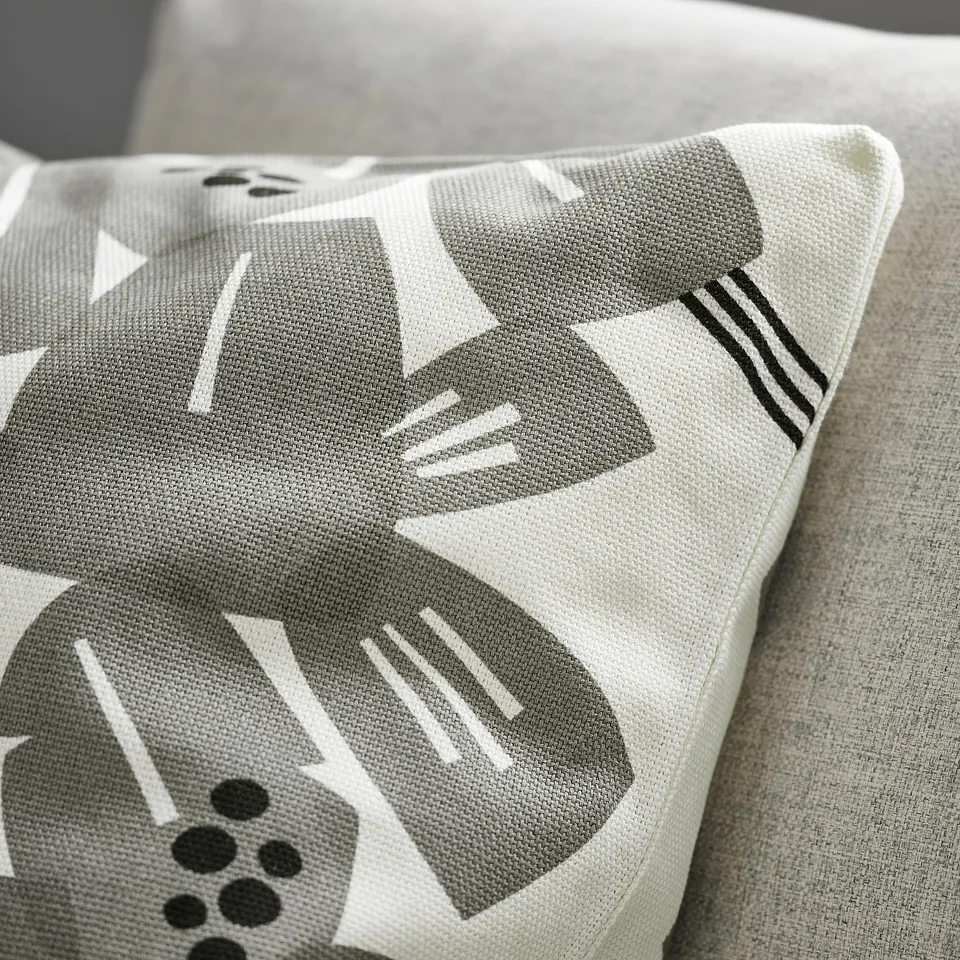 Square throw pillow with textured white and grey-green fabric, featuring playful leaf patterns. Boxed corners give it a structured look.