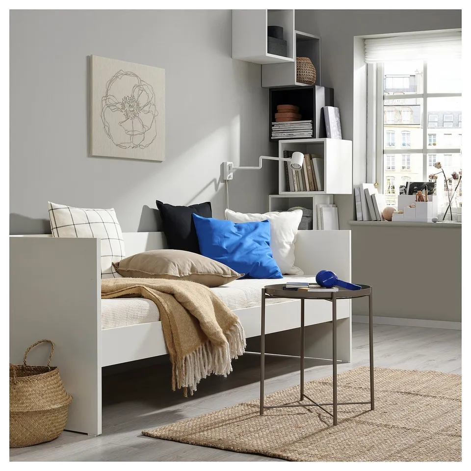 Modern white daybed with blue, beige, black cushions. Metal side table, city view.