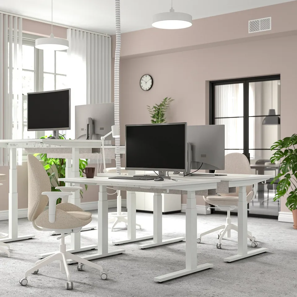 Modern office with MITTZON white sit/stand desks, ergonomic chairs, computers, and greenery. Desks larger than chairs, positioned under windows.
