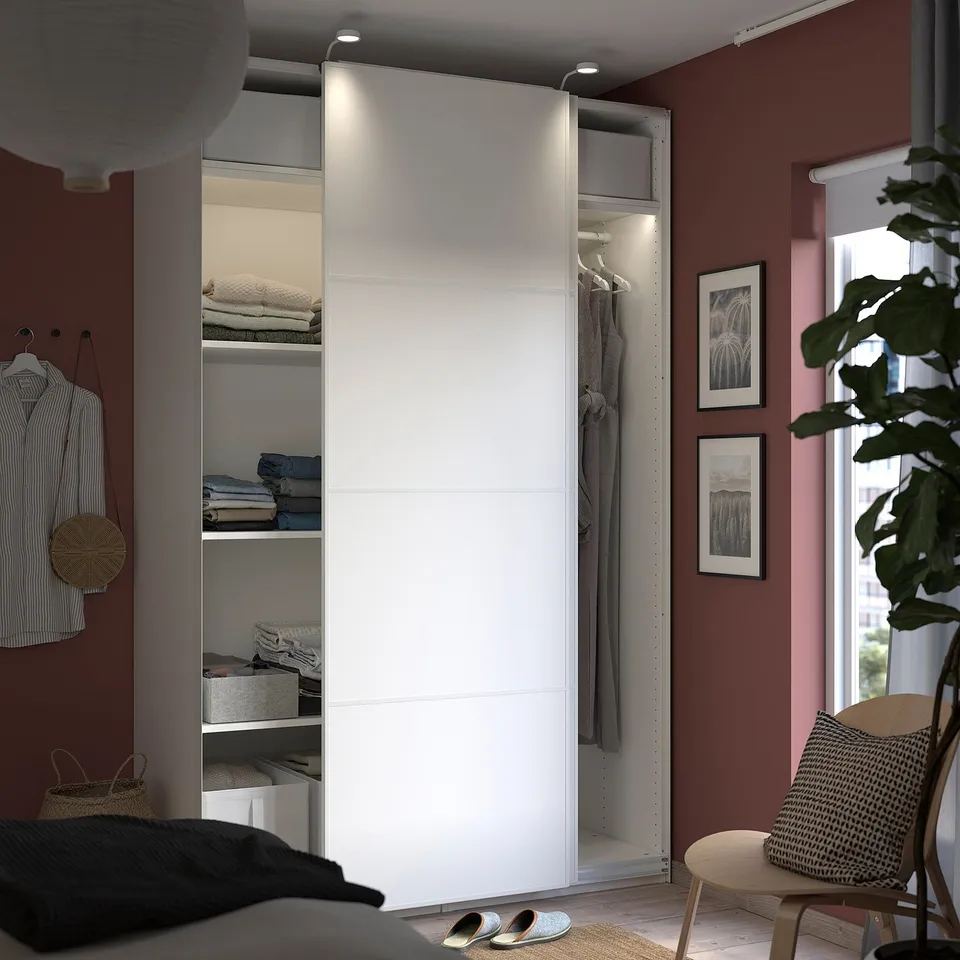 Modern bedroom with PAX wardrobe, glass door, lights, and shelves for clothes.