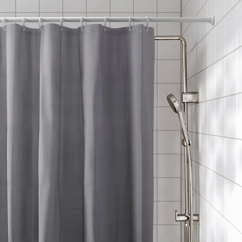 Grey shower curtain hanging from rod, with metallic shower head holder on tiled wall.