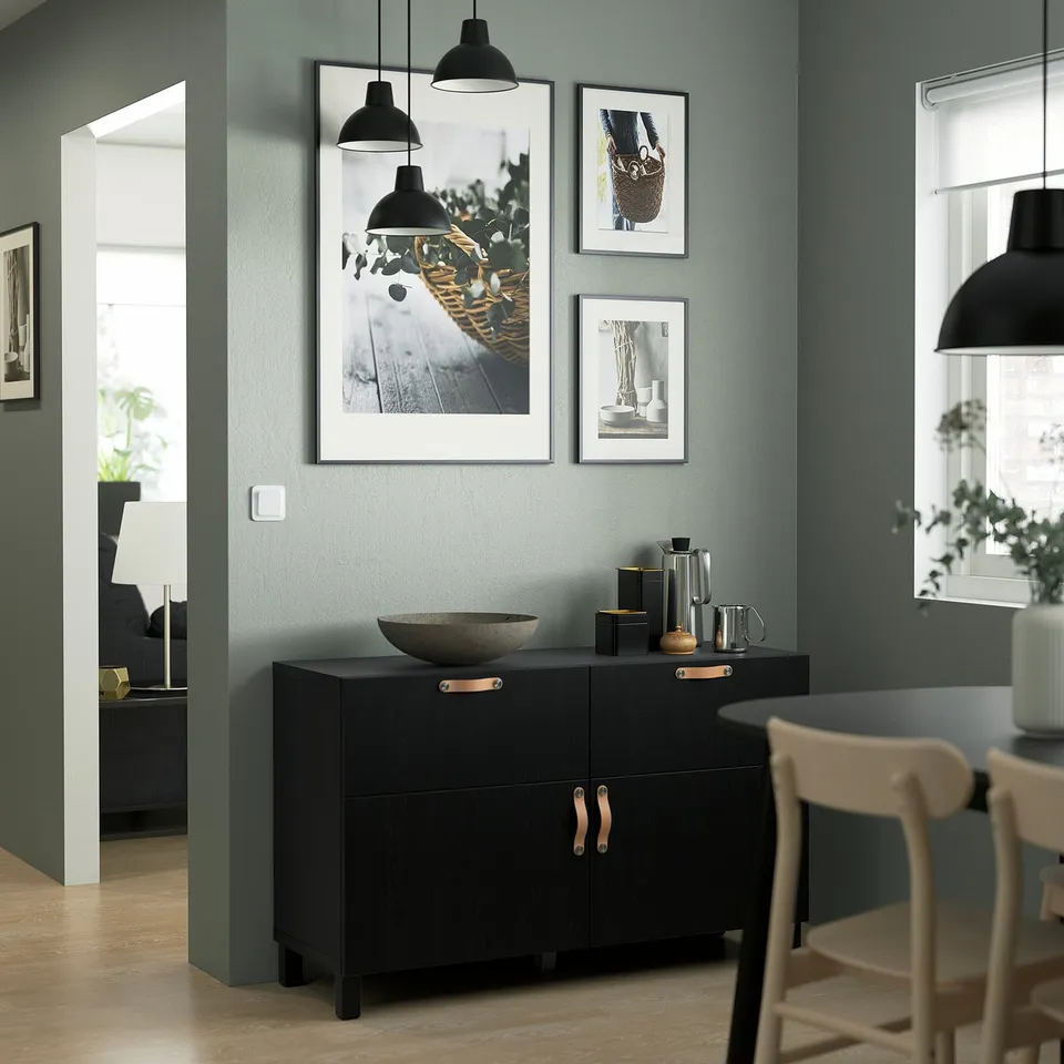 Black BESTÅ sideboard with shelves & drawers, green wall, pendant lamps, art, taller than beige chairs.