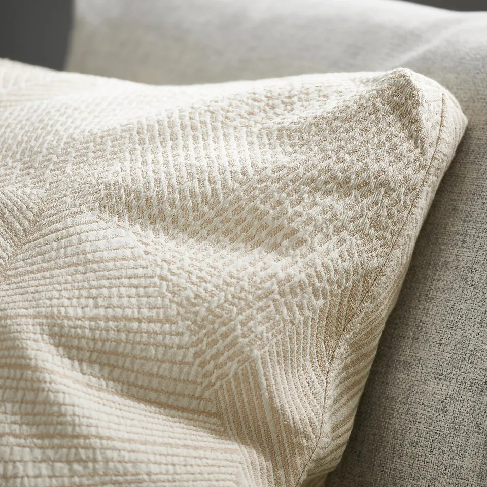 Close-up of intricately woven cushion cover with leaf-like pattern, showcasing textured jacquard weave and sturdy boxed corners.