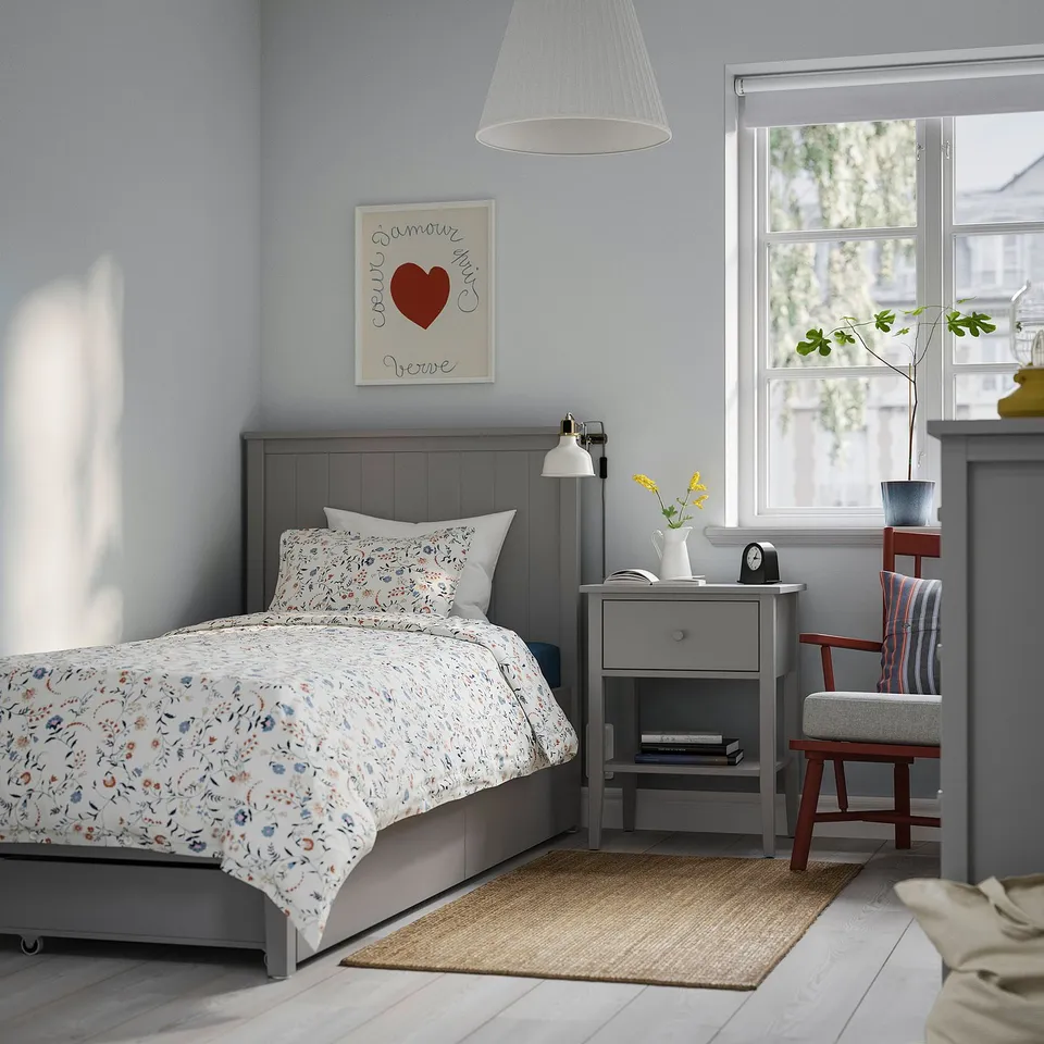Cosy bedroom with a grey GULLABERG bed, floral bedding, grey bedside table, striped chair, and wall art. Large window lets in natural light.
