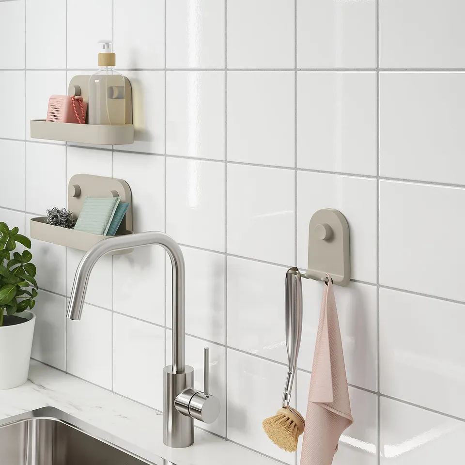 Kitchen sink with wall-mounted storage; towels and brush on hooks, soap dispenser on shelf; plant nearby.