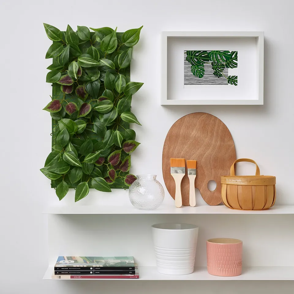 Wall-mounted FEJKA green plant panel with purple flowers, adding nature to decor. Eco-friendly, made from recycled plastic.