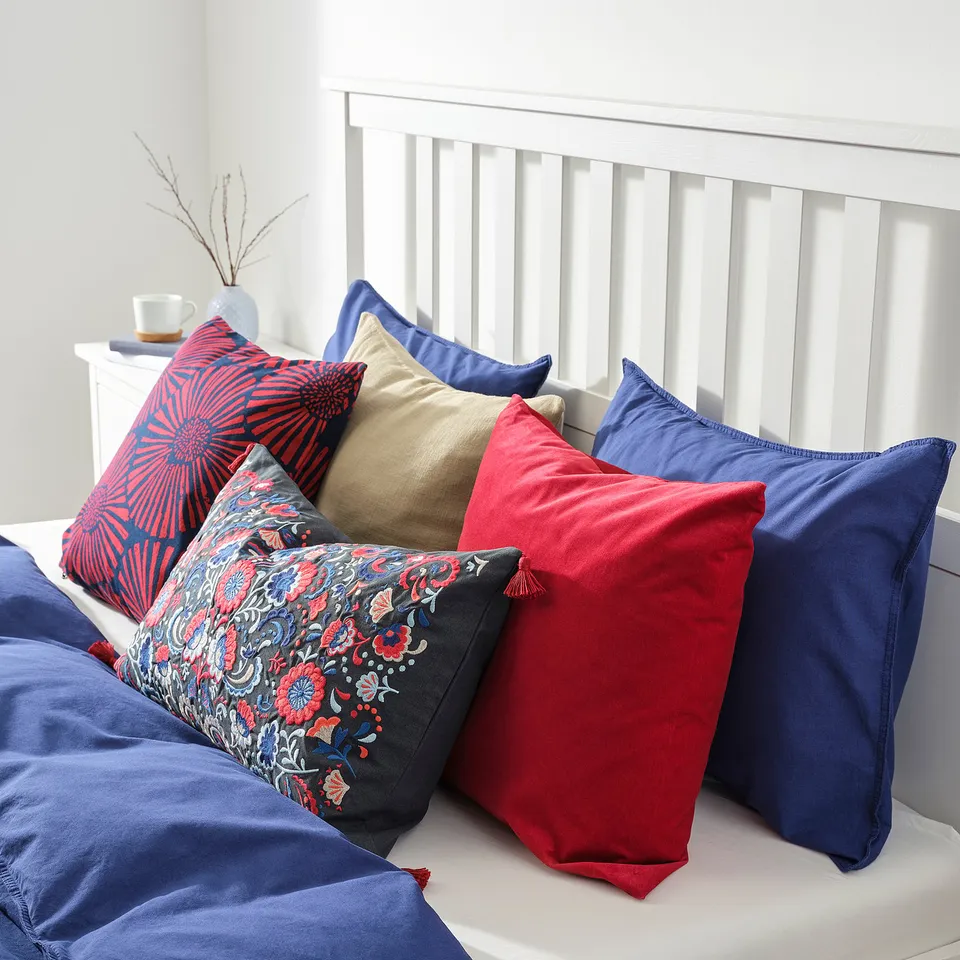 A bed with several colourful pillows; red, blue, and floral patterns for comfort.