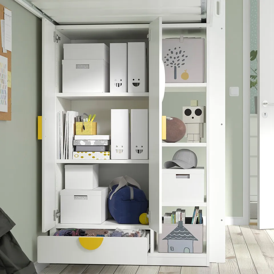 Open white cabinet with boxes, bags, books, and decorative items neatly organised. Shelves and drawers for storage.
