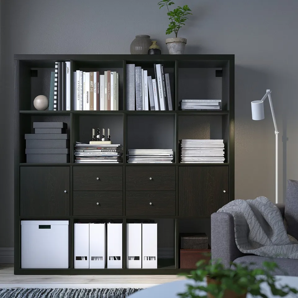 KALLAX black shelving unit with books, plants, and storage boxes, beside a grey sofa.