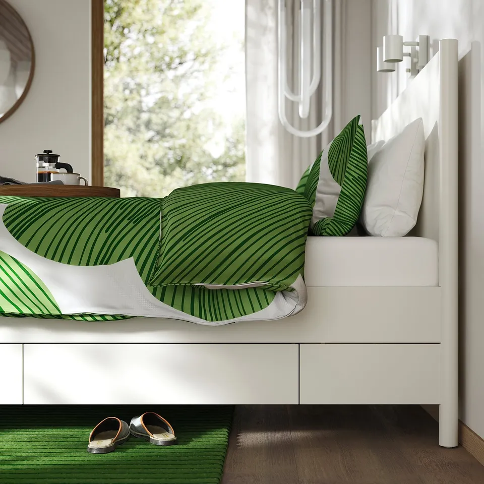 A modern bed with soft-close drawers in off-white, featuring adjustable bed sides. Green striped bedding and pillows enhance the sleek design.