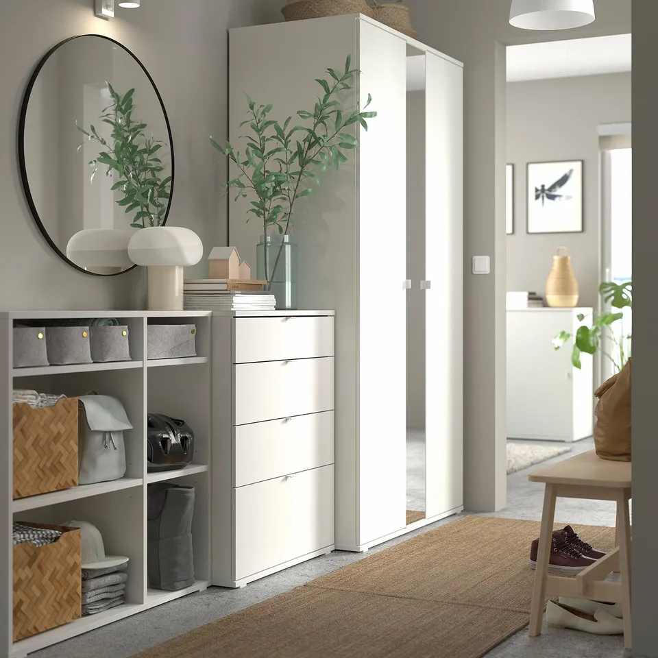 Modern entryway with white storage units and mirror, featuring green plants and a wooden bench.