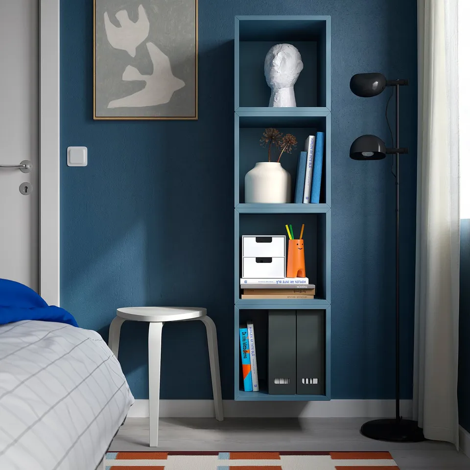 EKET blue wall-mounted shelves hold books, decor, beside cosy bed; minimalist design.