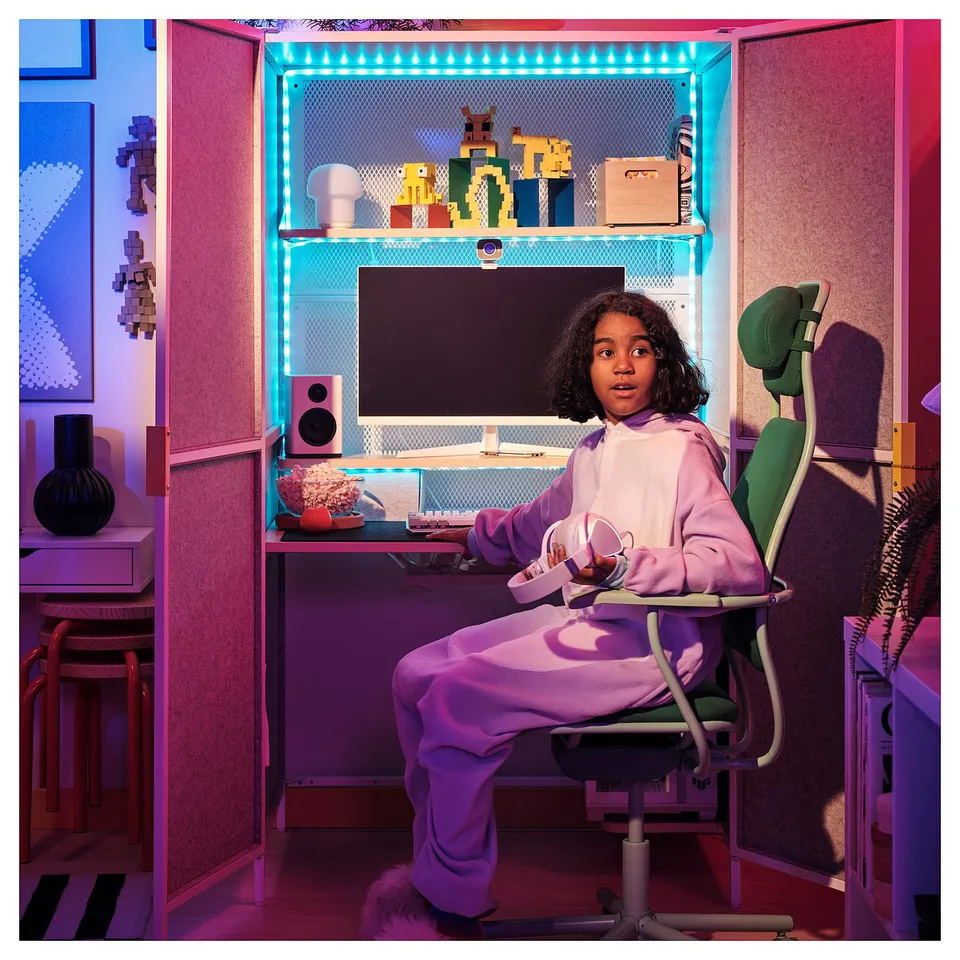Young child sits in an ergonomic gaming chair, adjusting height for comfort while playing on a well-lit desk with a computer and speakers.