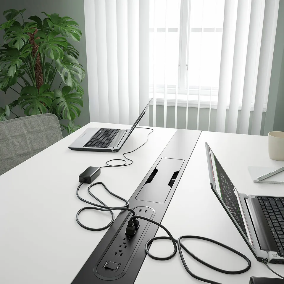Conference table with multiple laptops, power strips, and cables for collaborative work.
