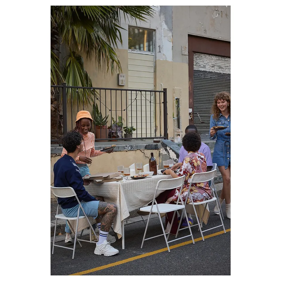 Group of people sitting at TORPARÖ outdoor dining set, enjoying food and drinks on a street, surrounded by buildings and palm trees.