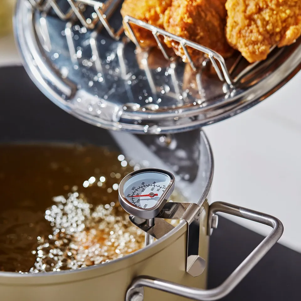 Silver pot with temp gauge frying food. Strainer holds fried items over oil.