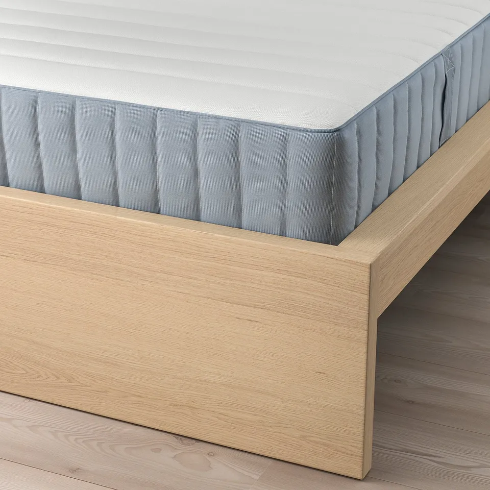 A close-up view of a corner of a MALM bed frame with slatted base and adjustable sides.