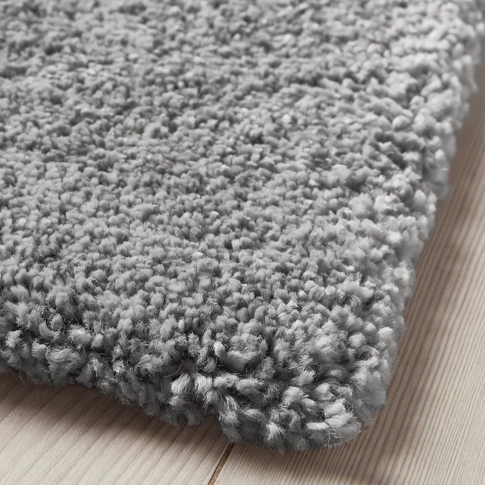 Close-up of a thick, soft, grey plush area rug. Showing texture, pile, and edge details.