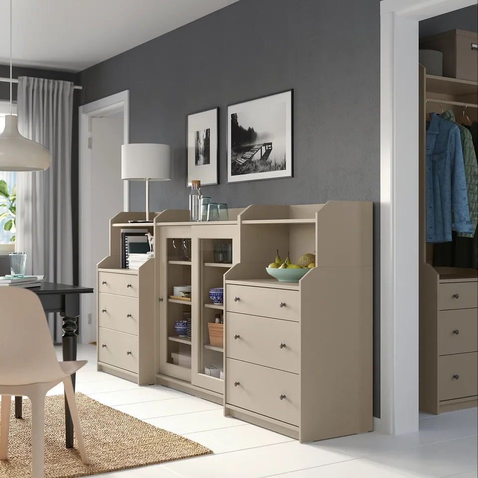 Modern room with beige HAUGA furniture set, including drawers, shelves, and cabinets with glass doors, against grey wall.