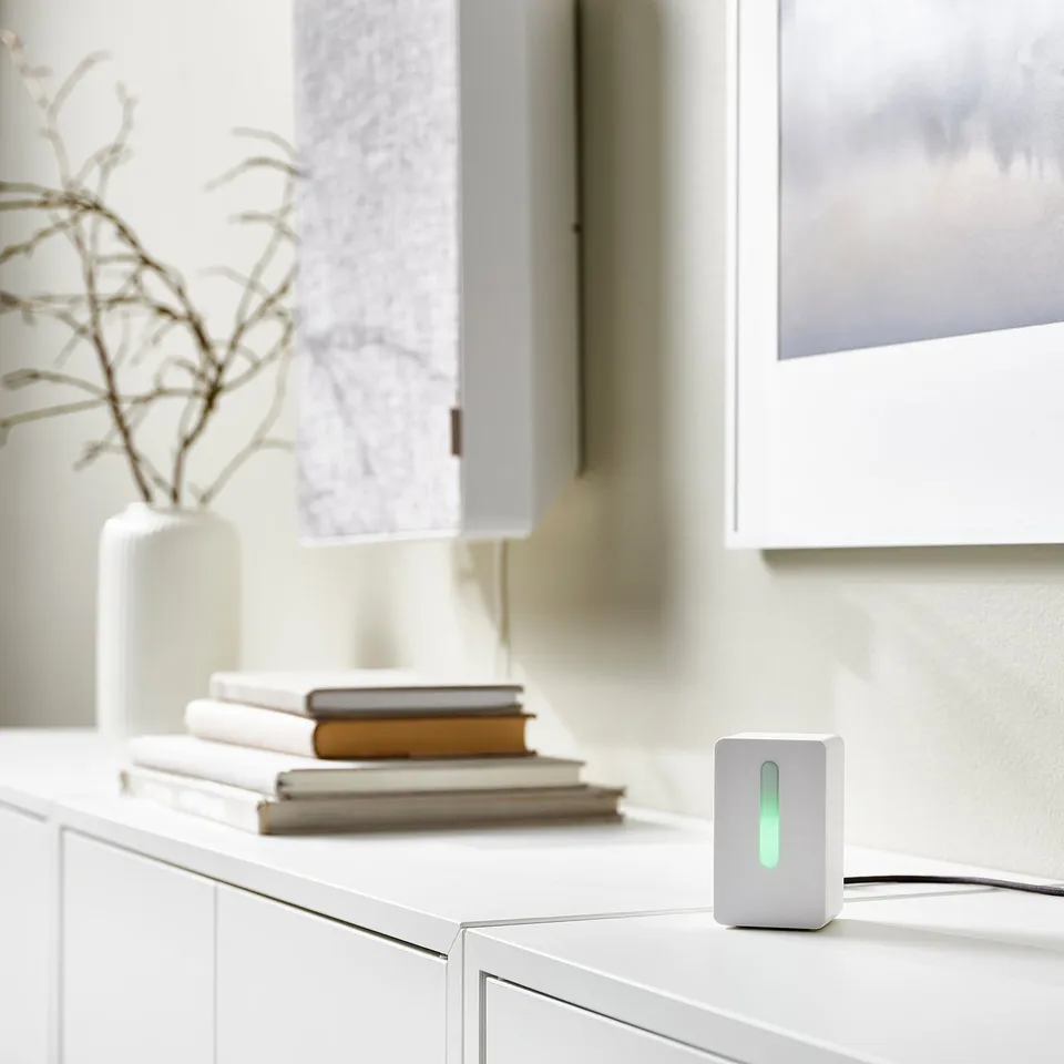 Small VINDRIKTNING white air quality sensor on cabinet, green light on, next to books and vase.