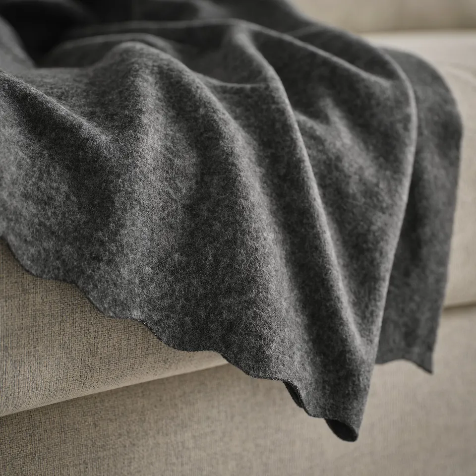 Dark grey fleece blanket draped on a beige couch, showcasing its soft and cosy texture.