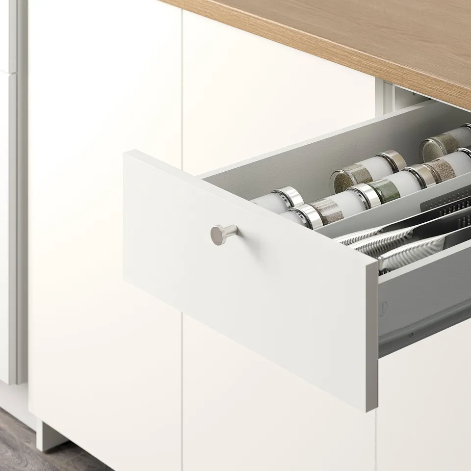 Open white kitchen drawer revealing organised spice rack with glass jars.