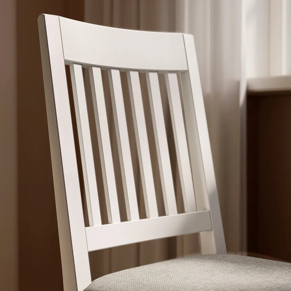 Modern white wooden chair with vertical slat back, upholstered seat in neutral fabric, placed indoors.