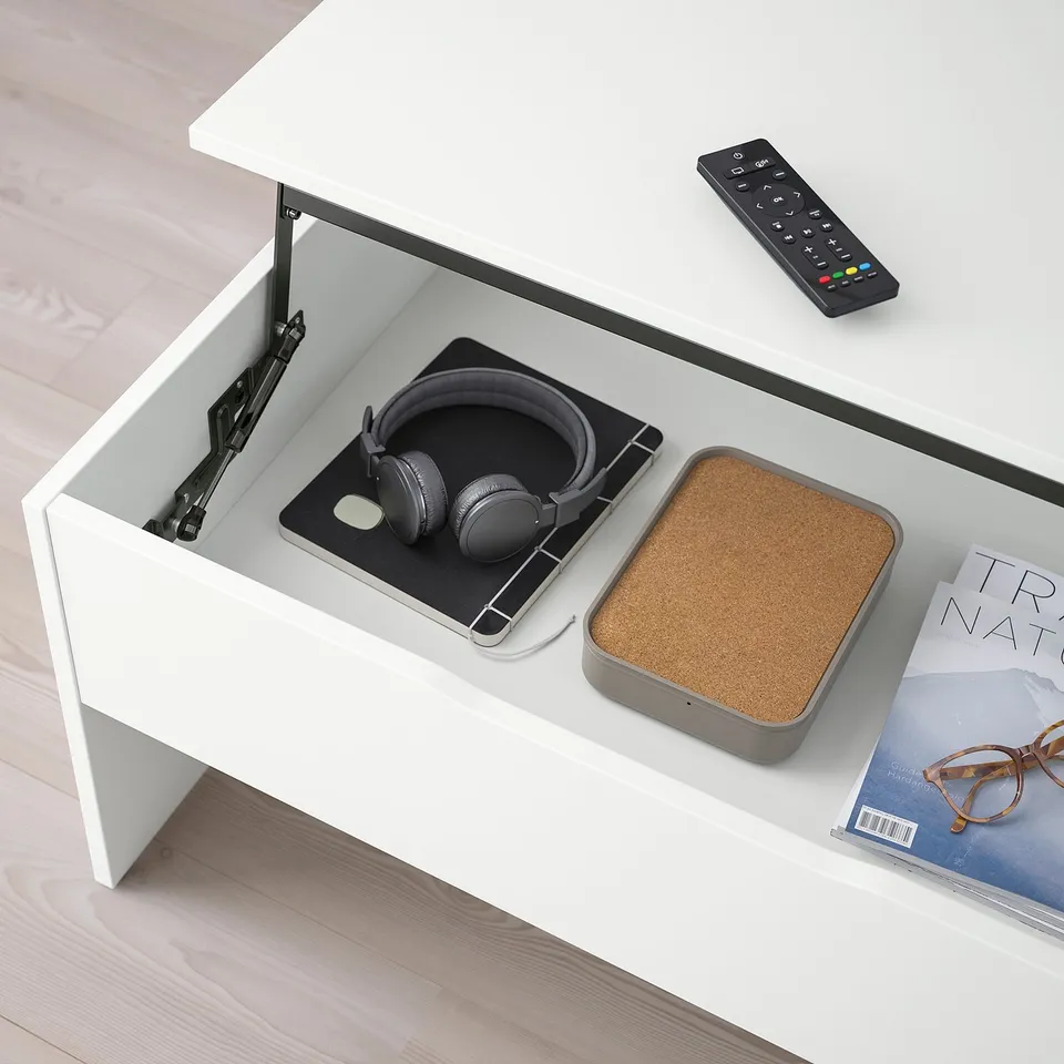 A modern coffee table with an adjustable top, showing a raised height, hiding storage inside with items like headphones and a remote.
