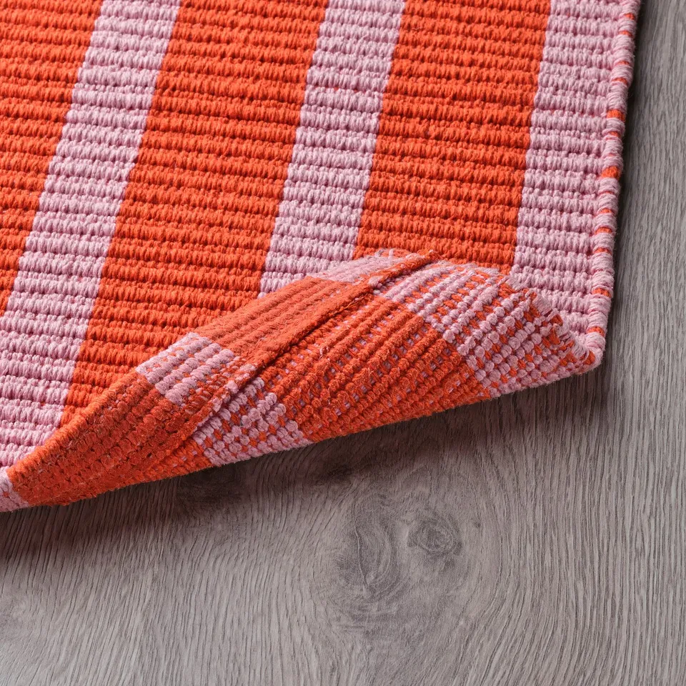 A colourful striped doormat, featuring orange and pink lines, lies on a wooden surface. The mats backing ensures it stays in place.