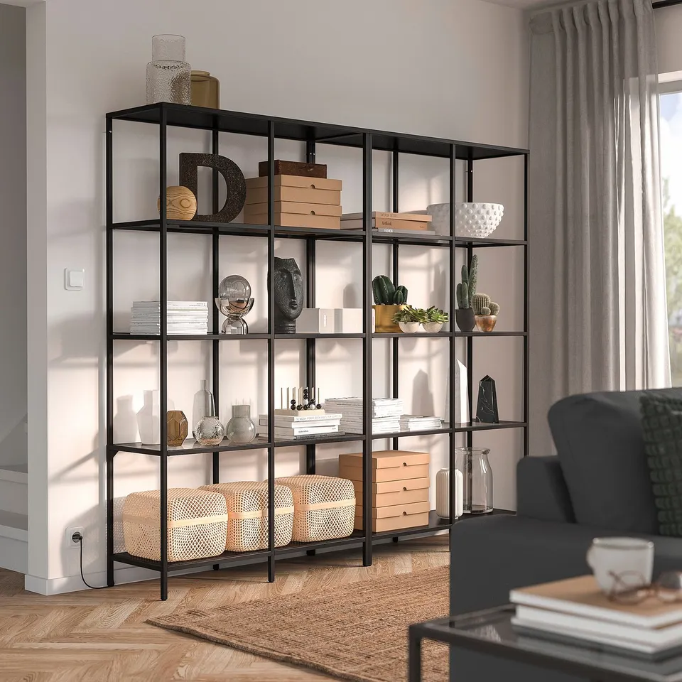 VITTSJÖ bookcase with dark metal & glass shelves, filled with decor & books in living room.