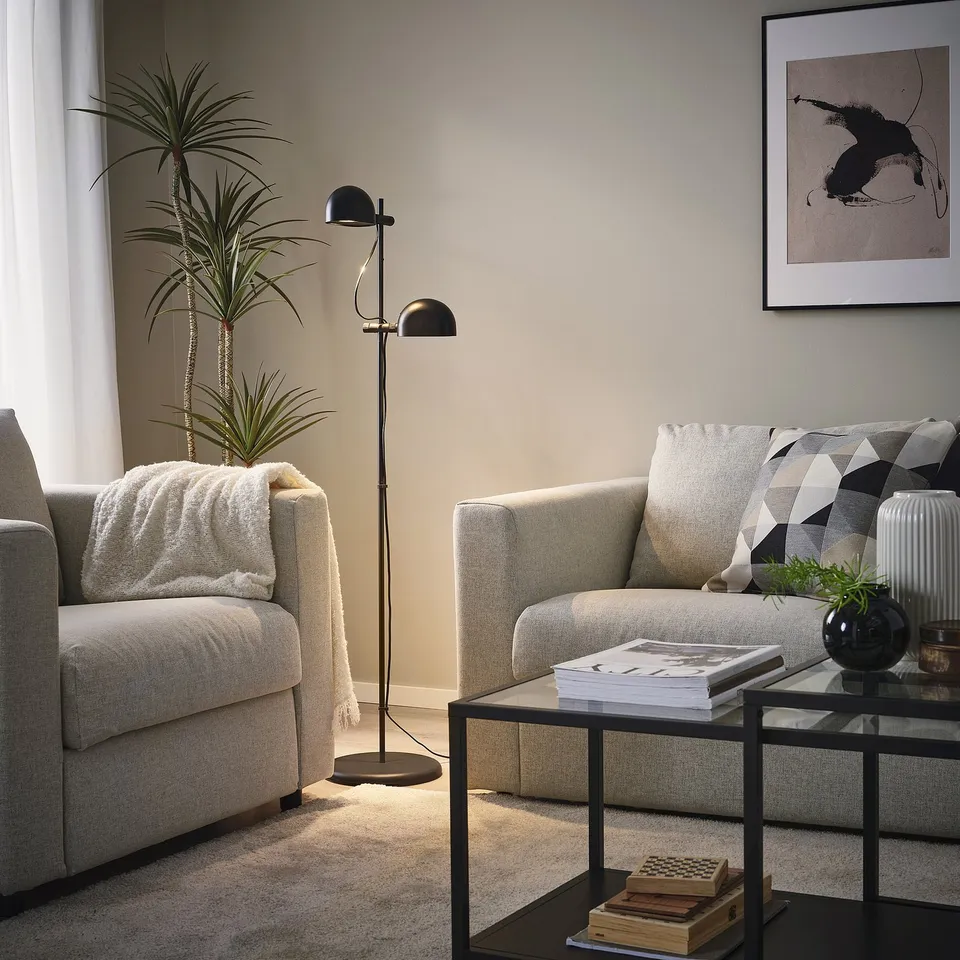 Grey armchairs, FOLKBÅT lamp, books & decor on coffee table, art & plant.
