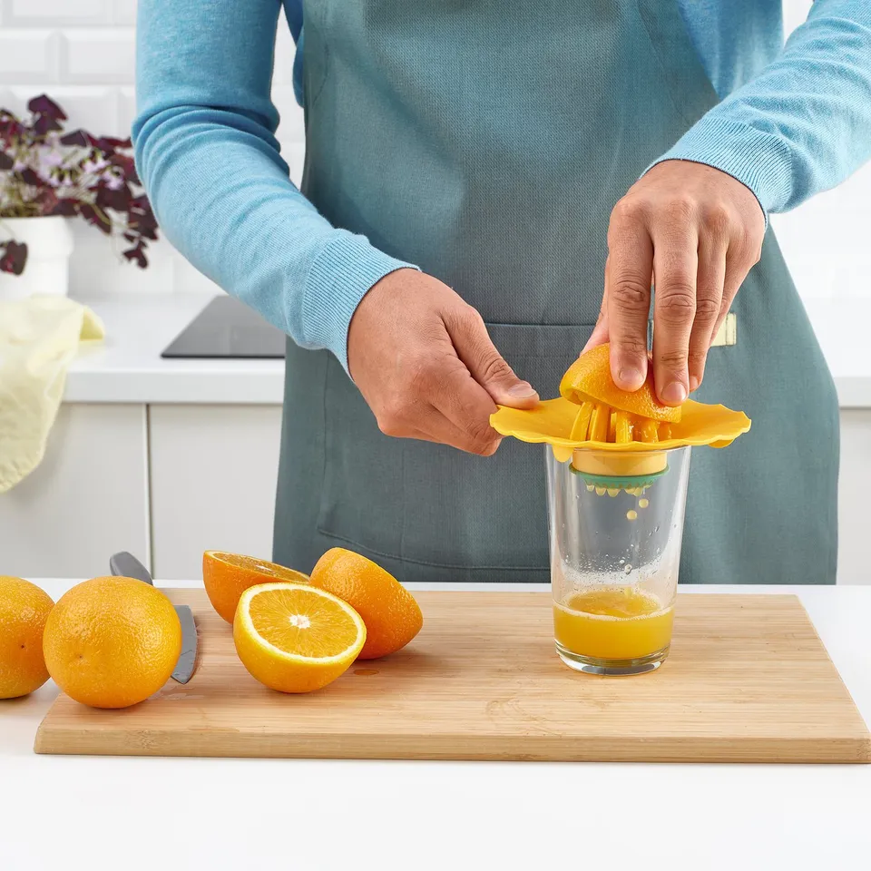 Person squeezing orange using yellow juicer into glass on wooden board.