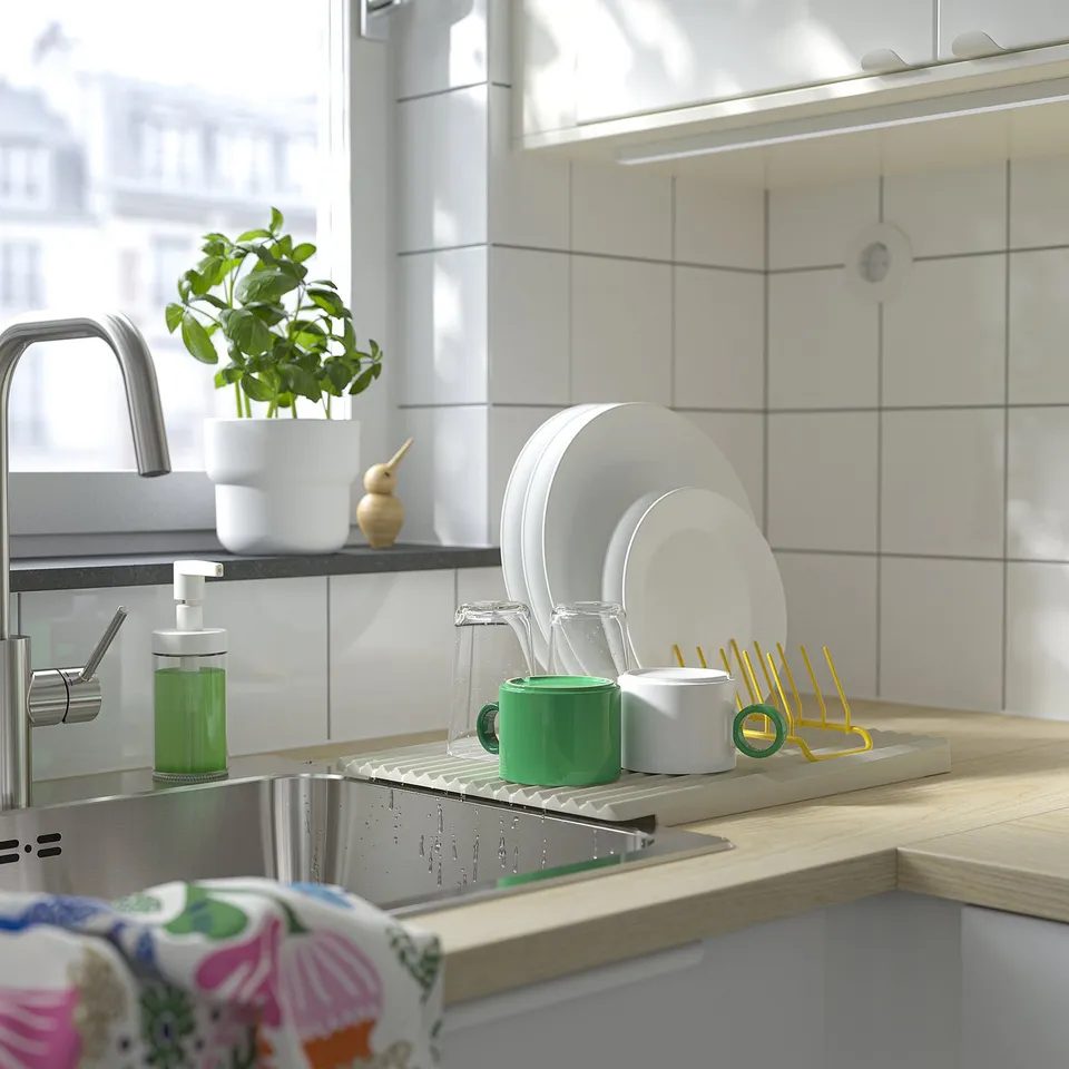Sink with dish drainer, cups, plates, plant, soap dispenser, and cloth.