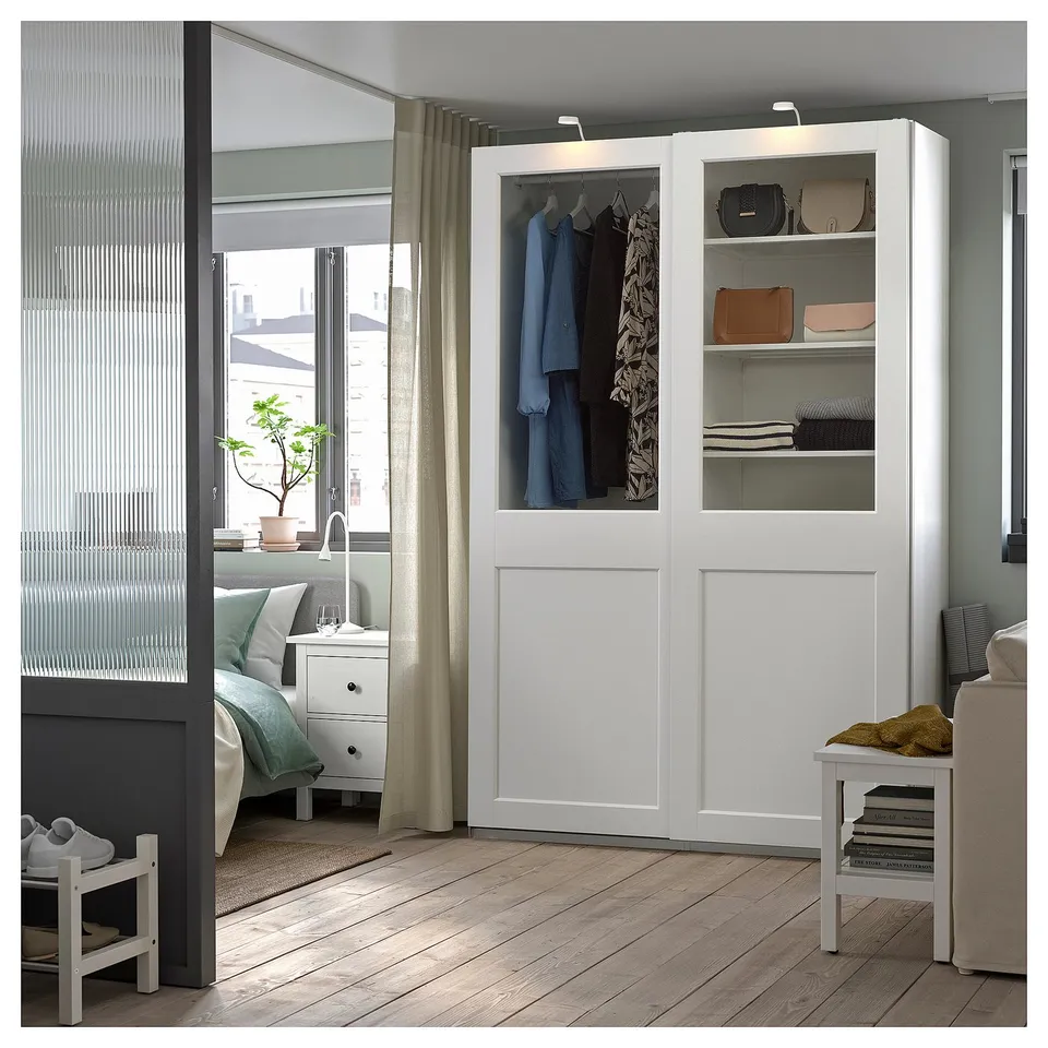 A modern white PAX wardrobe with glass doors, displaying clothes and accessories.