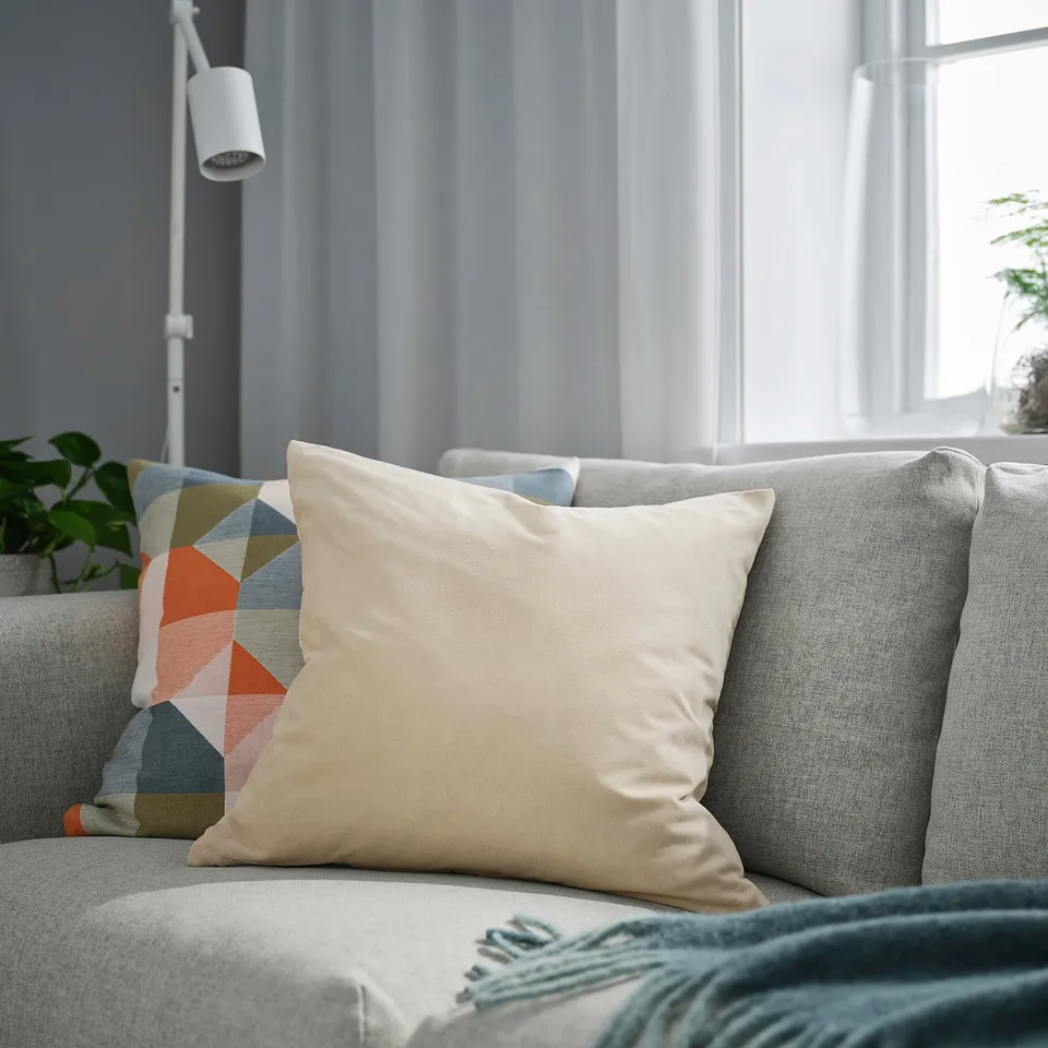 Beige cushion on grey sofa, multicoloured geometric pillow behind. Cosy living room with velvet texture.