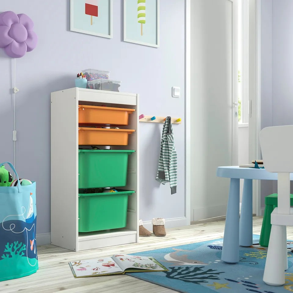 Childs room with white TROFAST storage unit, orange and green bins, next to blue table and chair set.