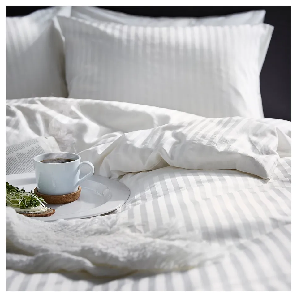 Beautiful white bed with NATTJASMIN striped duvet, plain pillows, breakfast tray, mug, plate, and toast.