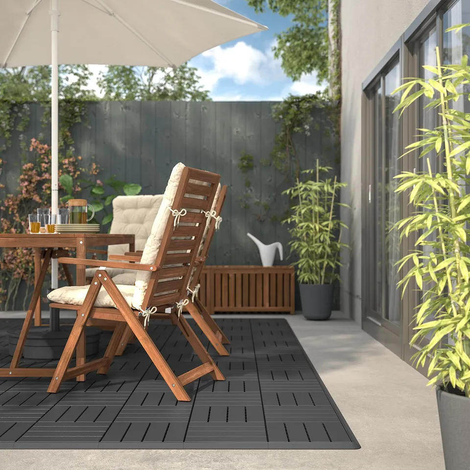 Outdoor patio with black RUNNEN decking, wooden chairs & cushions, plants, and large umbrella.