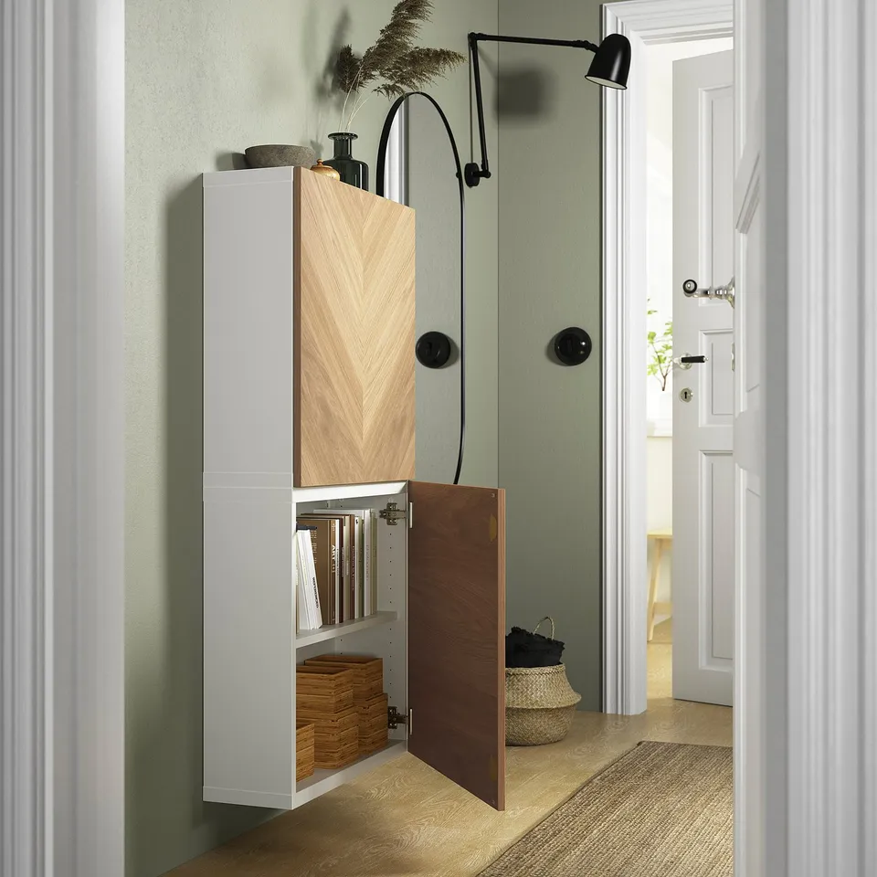 White cabinet with wooden doors open, showing shelves with books and baskets, mounted on green wall with adjustable shelf.