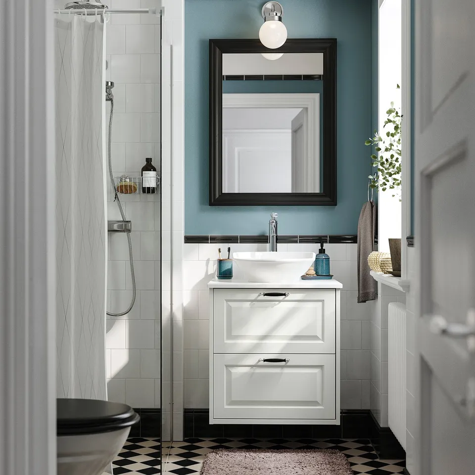 White TÄNNFORSEN vanity with basin, walk-in shower, bevelled edges, dark mirror, blue wall, glass shower door, black/white floor.