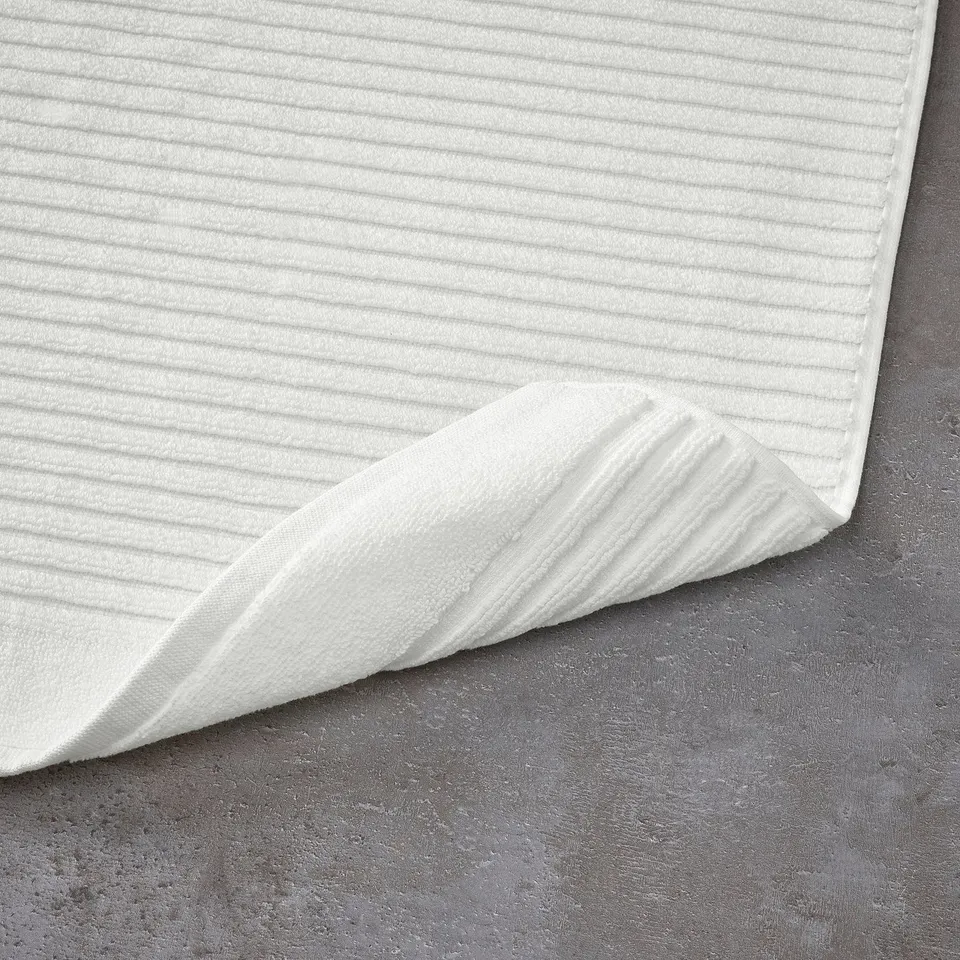 White bath mat laid flat, textured surface visible. Fast-drying, high-absorption cotton.