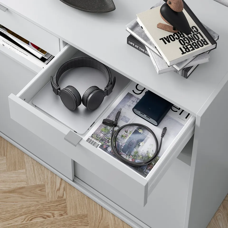 White desk drawer open, displaying black headphones, power bank, and coiled cable on a magazine.